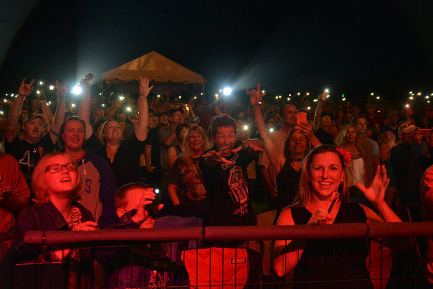 A smiling crowd of live music fans hold up the flashlights on their camera phones at a summer concert.