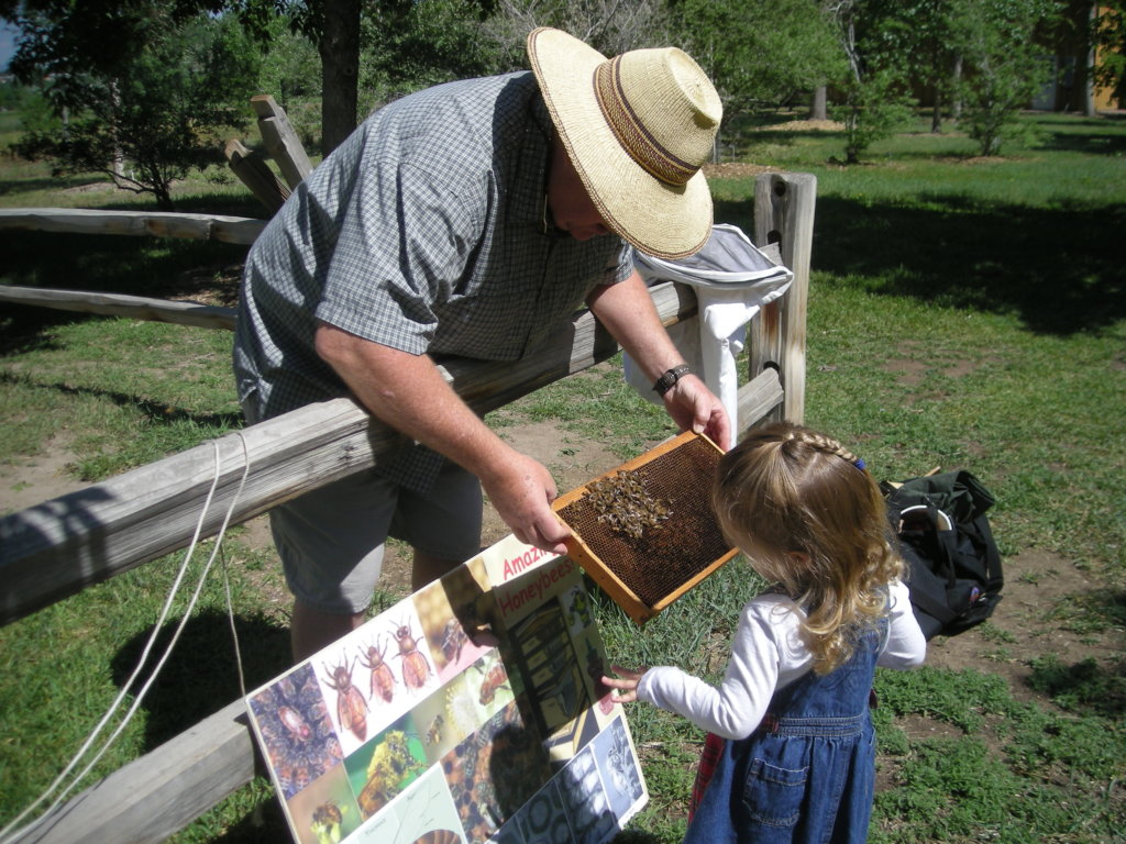 A beekeeper shows a child his honey bee hive.