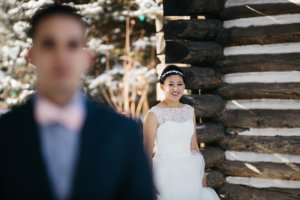 A bride reveals her wedding dress to her groom for the first time in front of a log cabin venue.
