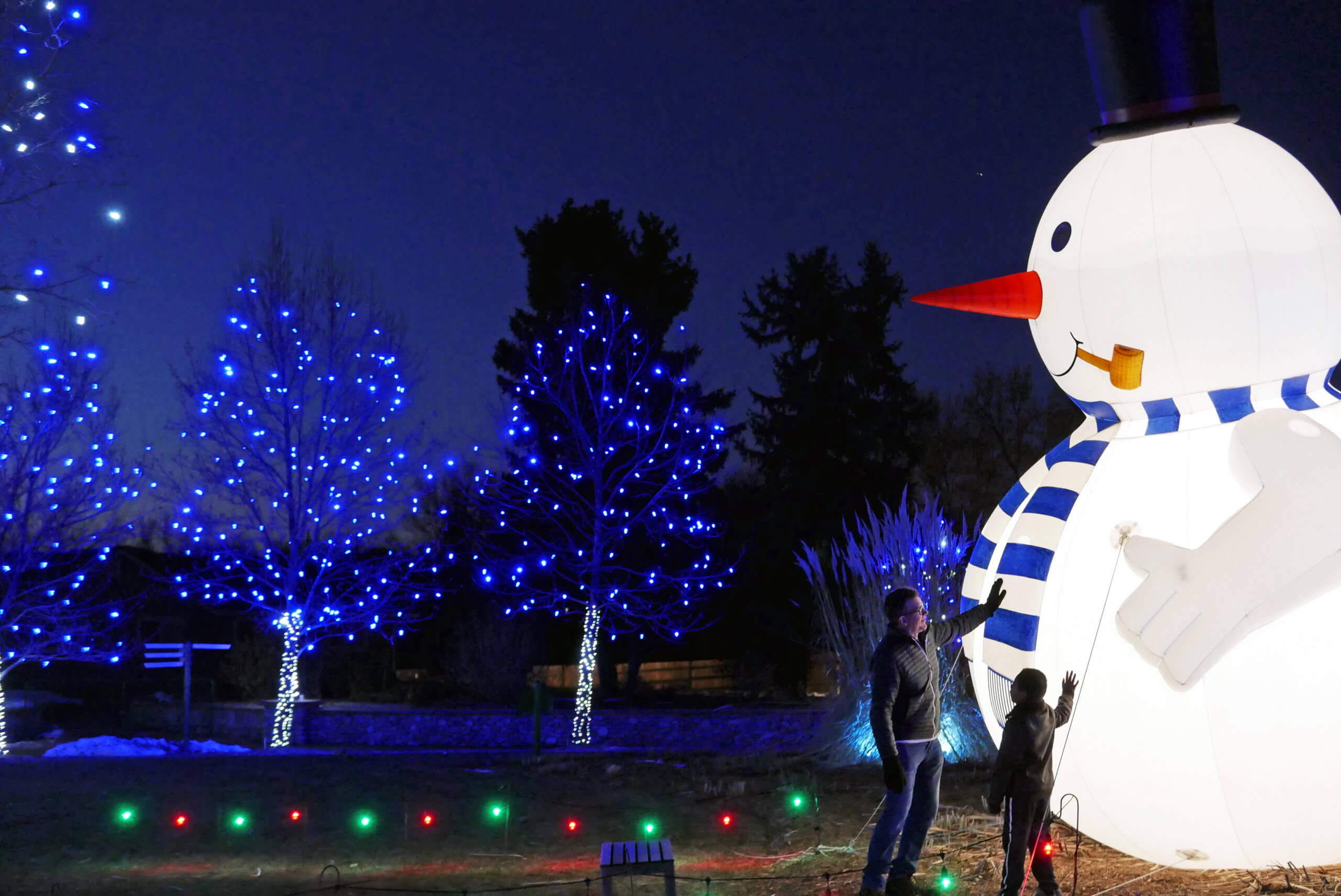 A Father and son rub the belly of a giant, glowing snowman
