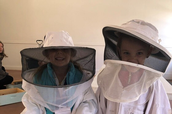 Two small children in beekeepers outfits including faceguards