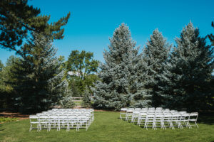60 White folding chairs in rows of 1 with a gap in the middle for people to walk through outdoors at Hudson Gardens