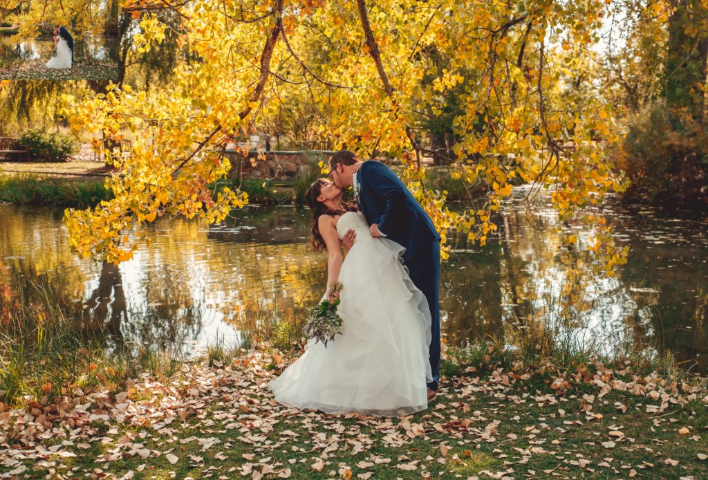 A man an a woman in wedding attire kissing outdoors