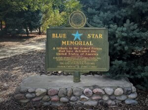 A green steel sign with a blue star and yellow text reading "Blue Star Memorial: I tribute to the Armed Forces that have defended the United States of America