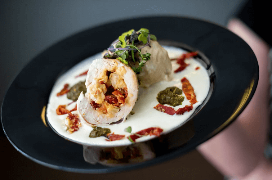 Black plate with garnished porchetta surrounded by a cream sauce.