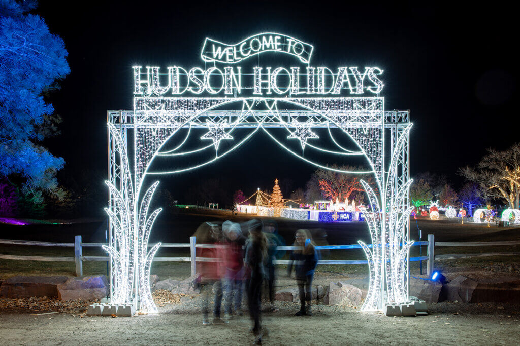 Long exposure photo of group standing under lighted ornate 'Welcome To Hudson Holidays' arch