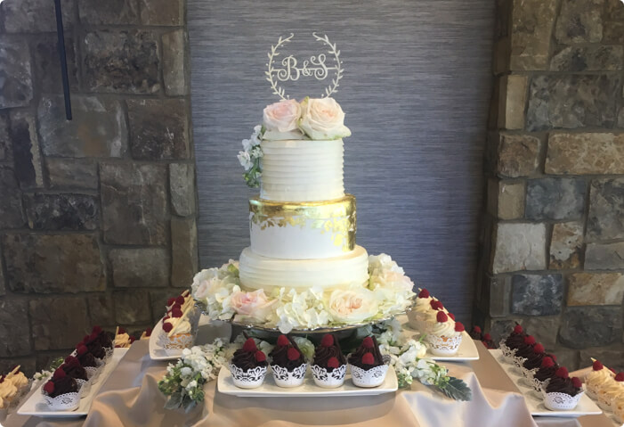 3-tier white wedding cake with pink florals and chocolate cupcakes surrounding